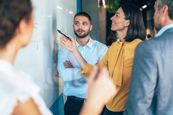Three coworkers discussing plans written on a glass dry erase board