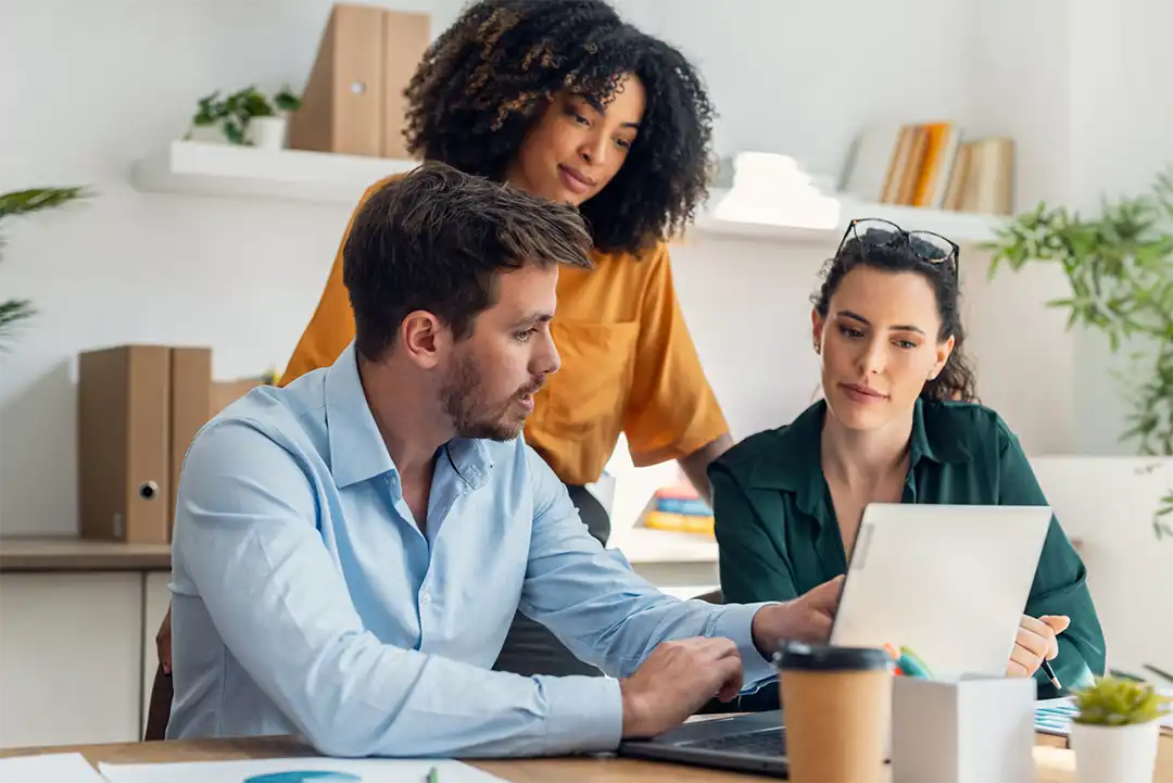Three coworkers discussing plans written on a glass dry erase board